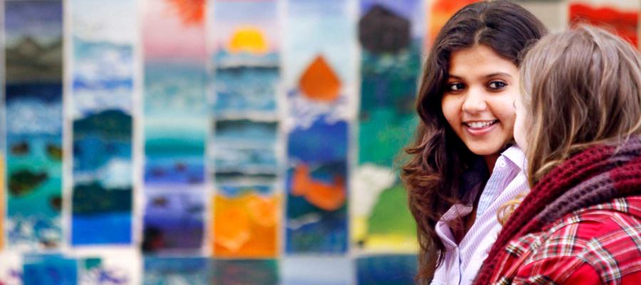 Two students talking in front of a colourful mural