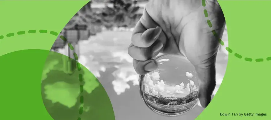 Hand holding a glass ball reflecting the sky