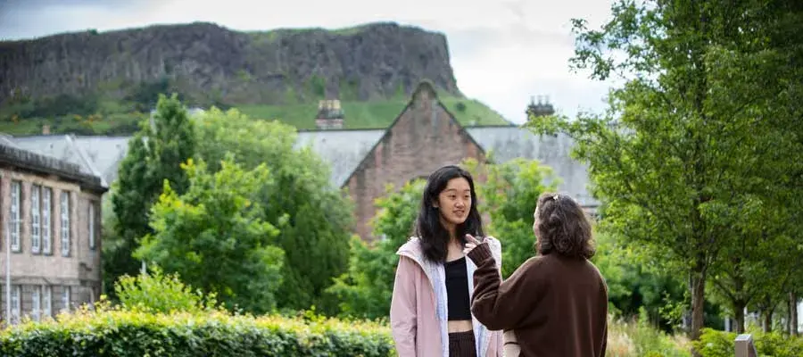 Two students talking in the quad with Paterson's land and Arthur's Seat in the background