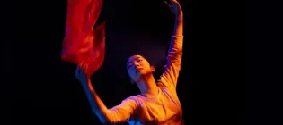 Dancer holding a red piece of fabric on a black background