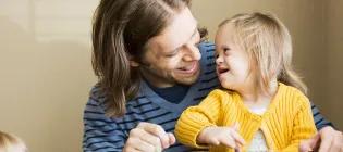 Father (30s) playing with daughter (2 years) who has down syndrome. Using digital tablet.