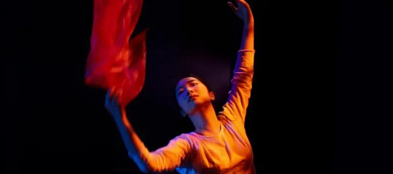 Dancer holding a red piece of fabric on a black background