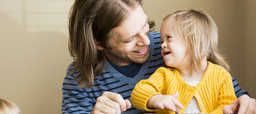 Father (30s) playing with daughter (2 years) who has down syndrome. Using digital tablet.