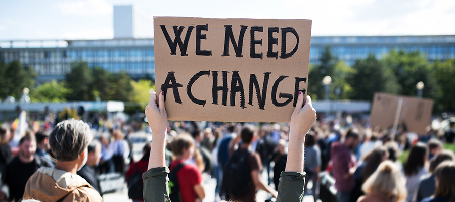 Protesting crowd holding a sign that says 'We need a change'