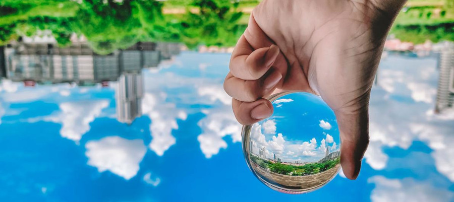 Hand holding a glass ball that's reflecting the sky and clouds